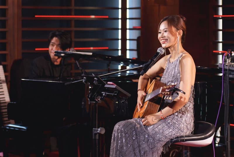 Jaya Lee with a guitar on a lounge stage, a pianist at a grand piano behind her
